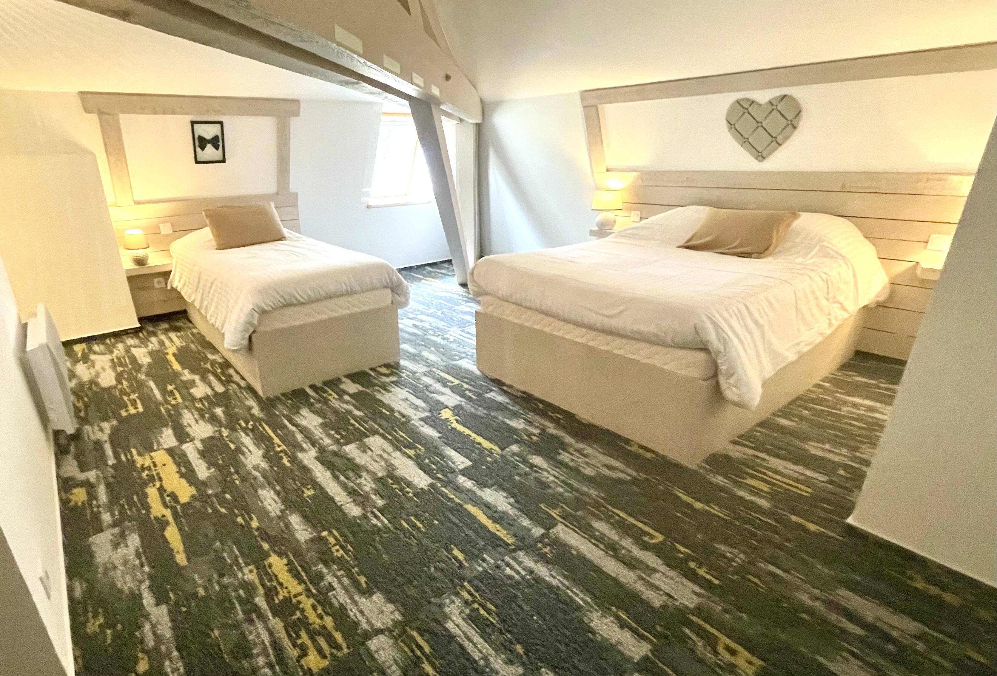 Una habitación de hotel con dos camas, alfombra estampada y una decoración de corazón en la pared.