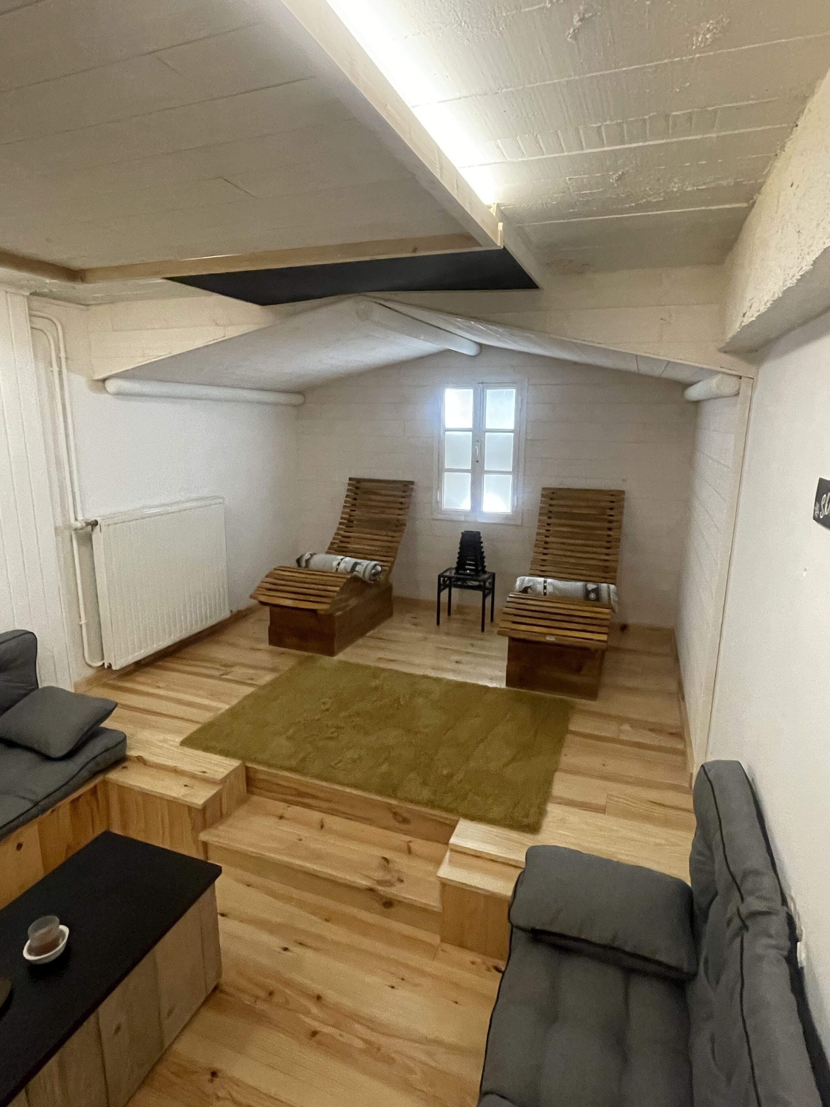 Ein Loft-Zimmer mit Holzboden, zwei Holzbänken, einem kleinen Tisch, einem grauen Sofa und einem Fenster.