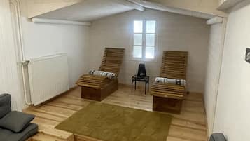 Ein Loft-Zimmer mit Holzboden, zwei Holzbänken, einem kleinen Tisch, einem grauen Sofa und einem Fenster.