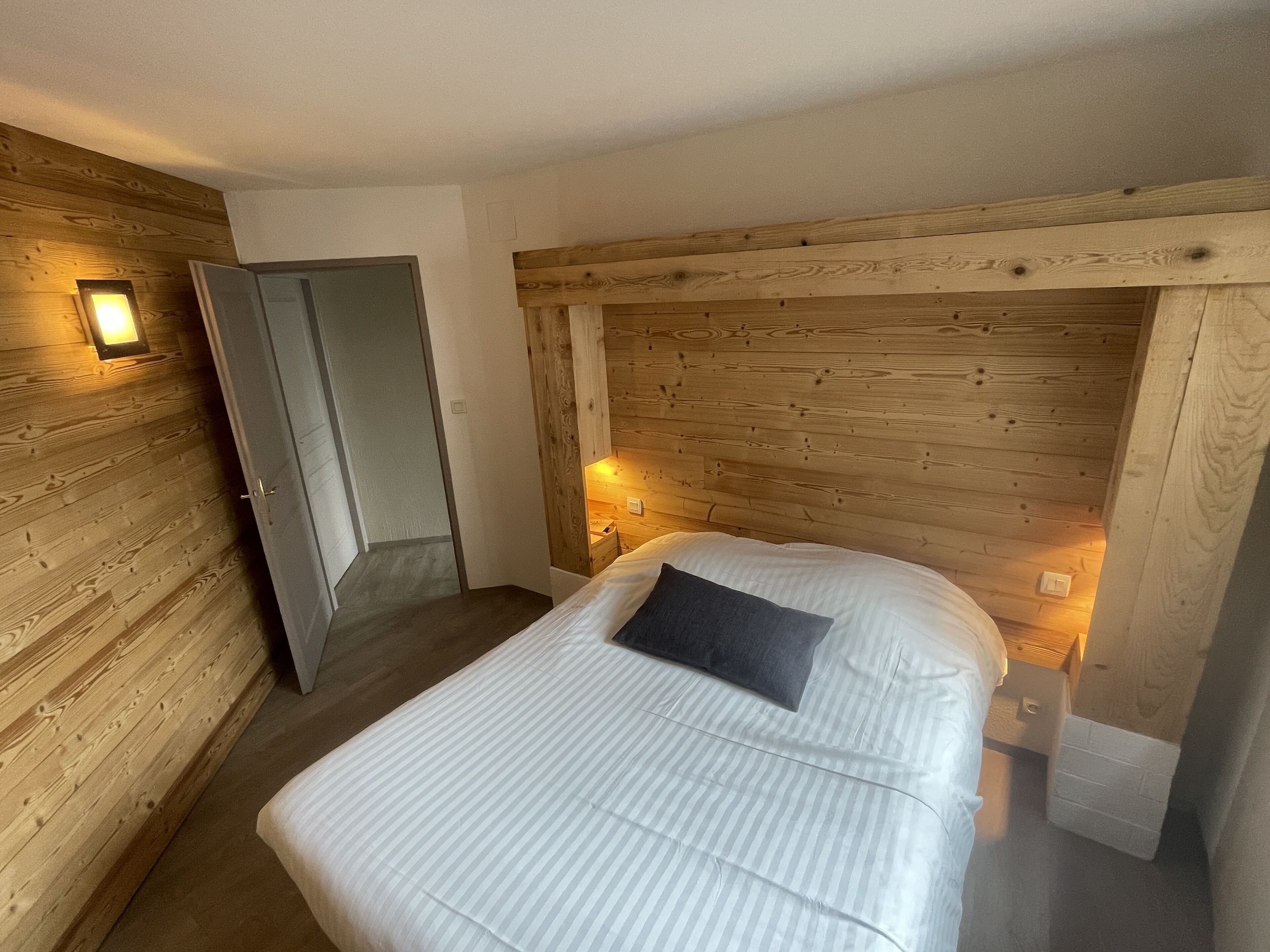 A bedroom with a wooden headboard, a bed with white bedding, and two wall-mounted lights.