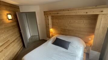 A bedroom with a wooden headboard, a bed with white bedding, and two wall-mounted lights.