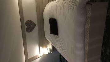 A bed with a white mattress and pillows, a small black object on the bed, and a wall-mounted light fixture.