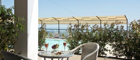 Een balkon met rieten stoelen, een glazen tafel en uitzicht op een zwembad.