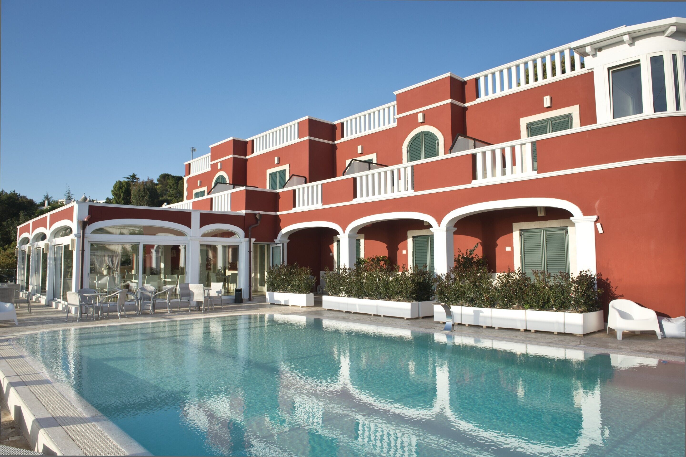 A poolside area with a clear blue pool, white lounge chairs, and a red building with white trim and green shutters.