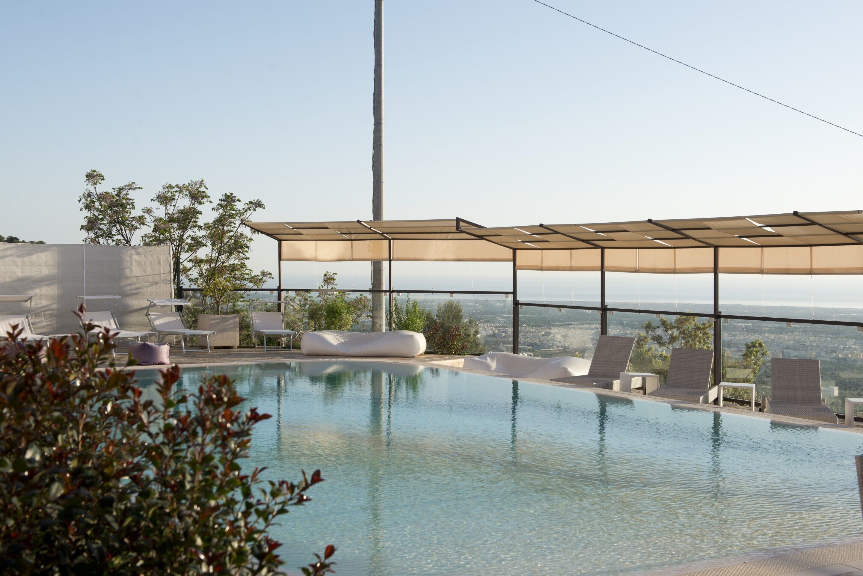 An infinity pool with lounge chairs and a canopy, overlooking a scenic view.