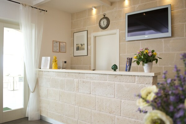 A reception area with a brick wall, a clock, a flat-screen TV, and a vase with flowers.