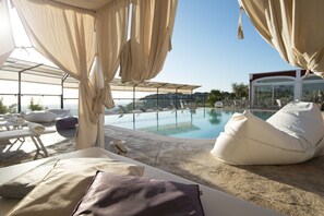 A poolside lounge area with sun loungers, a large bean bag, and a view of the pool and distant buildings. - Al Mirador Resort (Fasano)