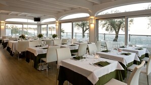 Un restaurant amb diverses taules preparades per dinar, grans finestres que donen vista al mar i un disseny interior modern.