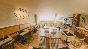 Interior de un restaurante con varias mesas y sillas, una zona de bar y una pared con el nombre 'RAÍCES COCINA LOCAL'.