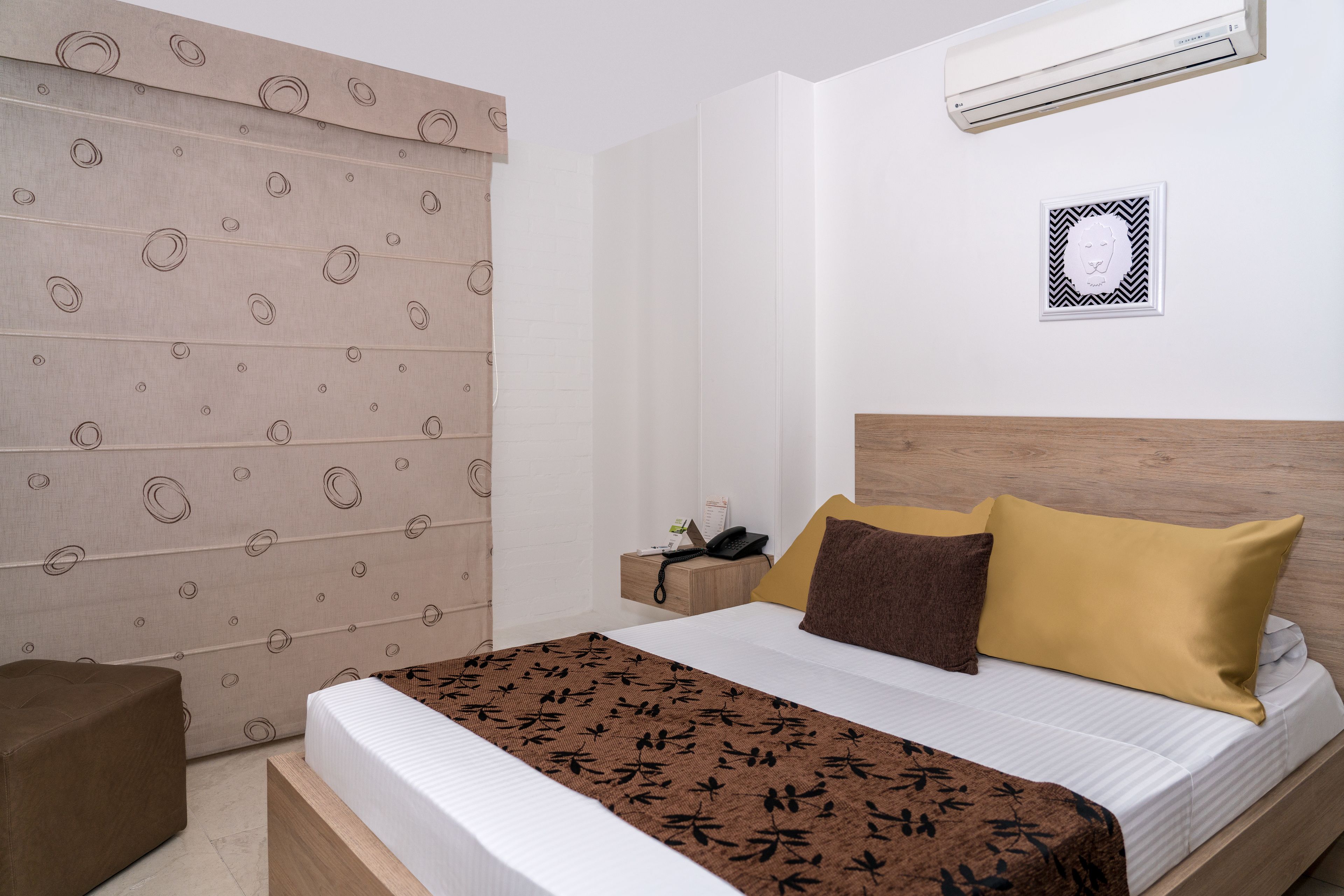 A neatly arranged hotel room with a bed, bedside table, and a wall-mounted air conditioner.