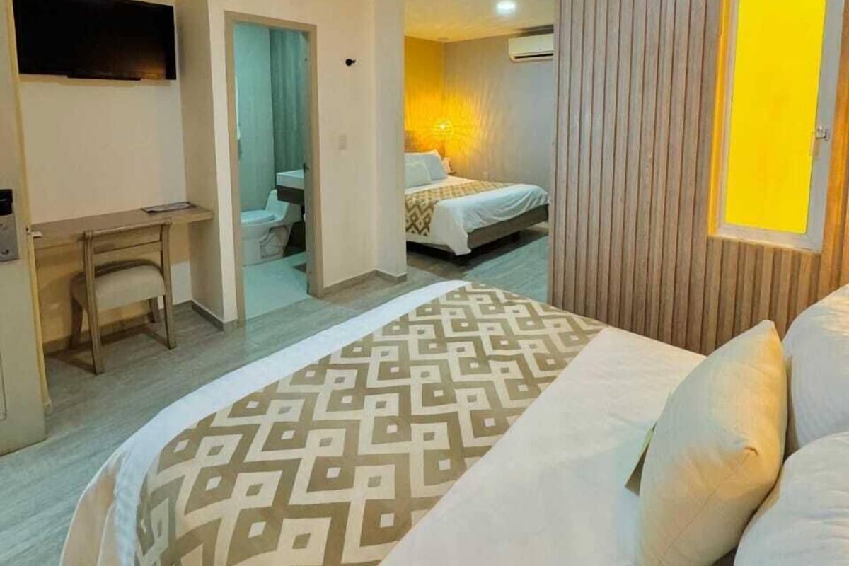 A hotel room with a bed, a desk, a television, and a bathroom visible through an open door.
