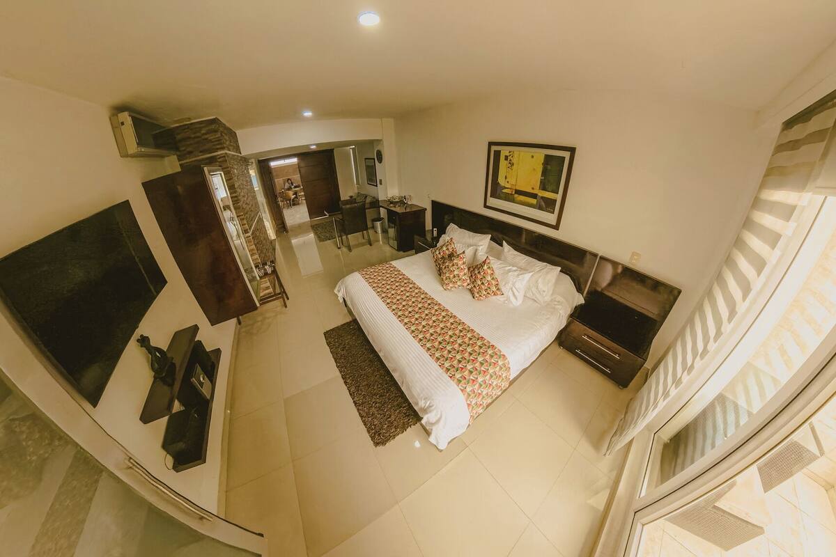 A bedroom with a bed, bedside tables, a desk, a chair, and a large window.