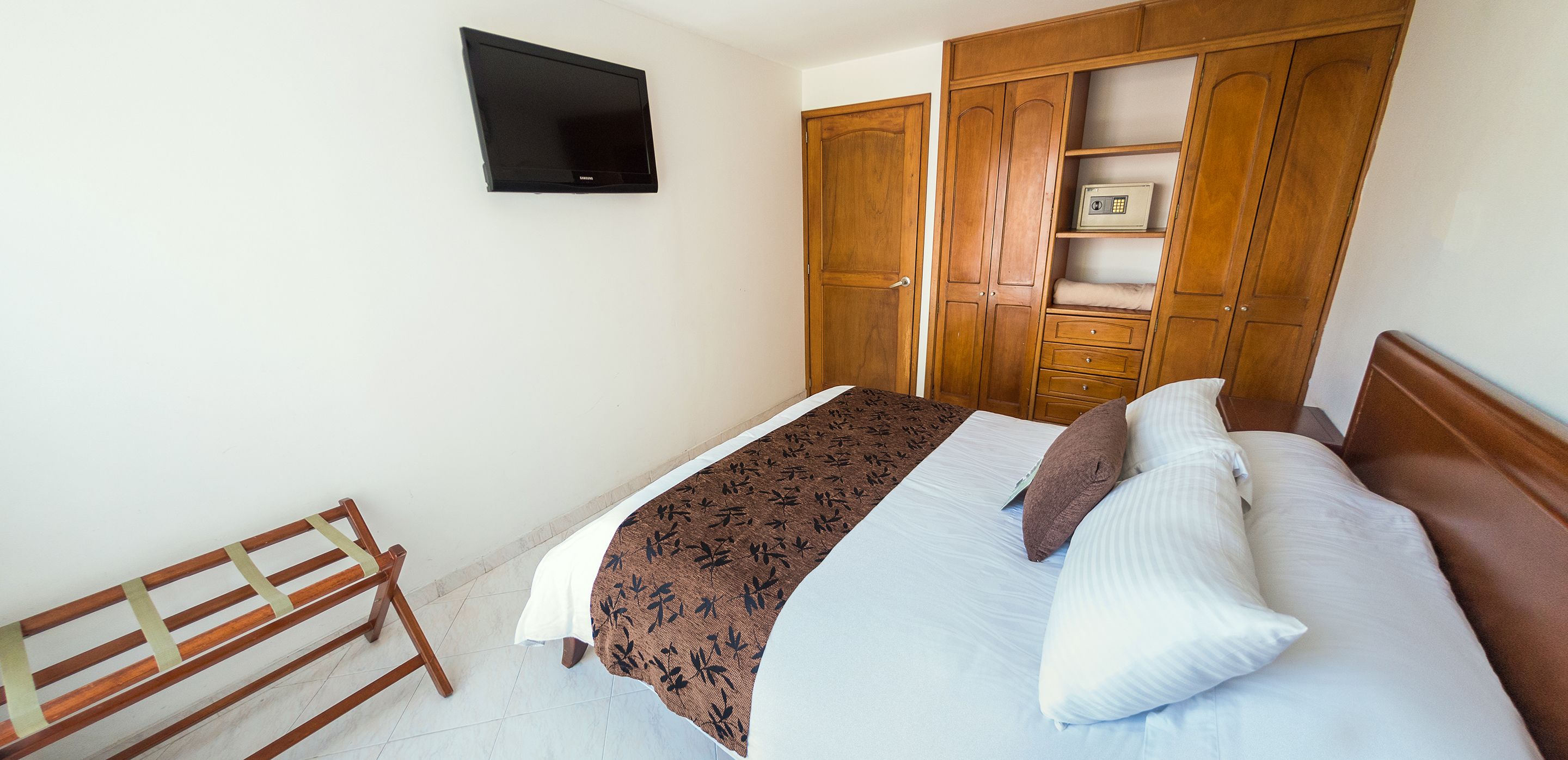 Ein Schlafzimmer mit einem Bett, einem Holzschrank und einem an der Wand montierten Fernseher.