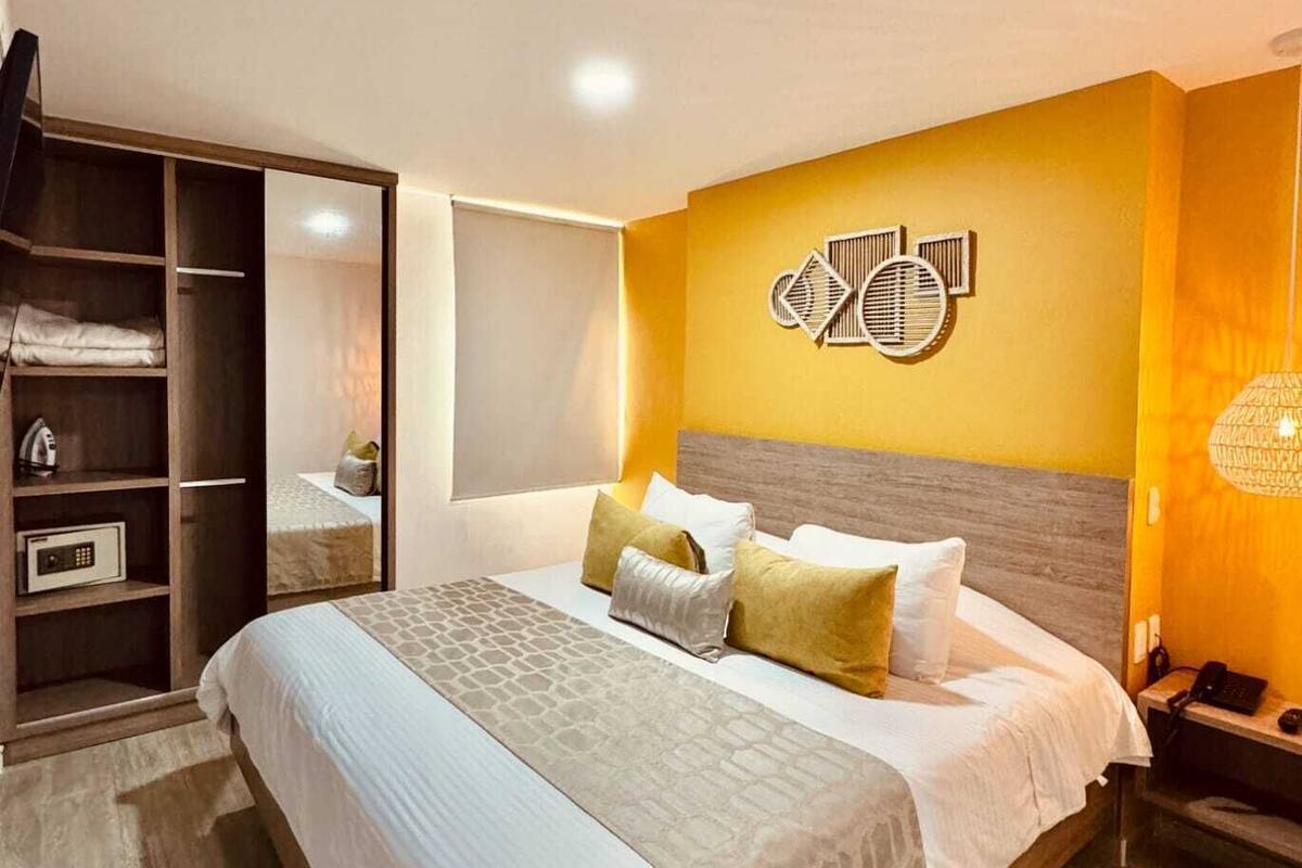 A hotel room with a bed, a wardrobe, a nightstand, and a wall-mounted artwork.