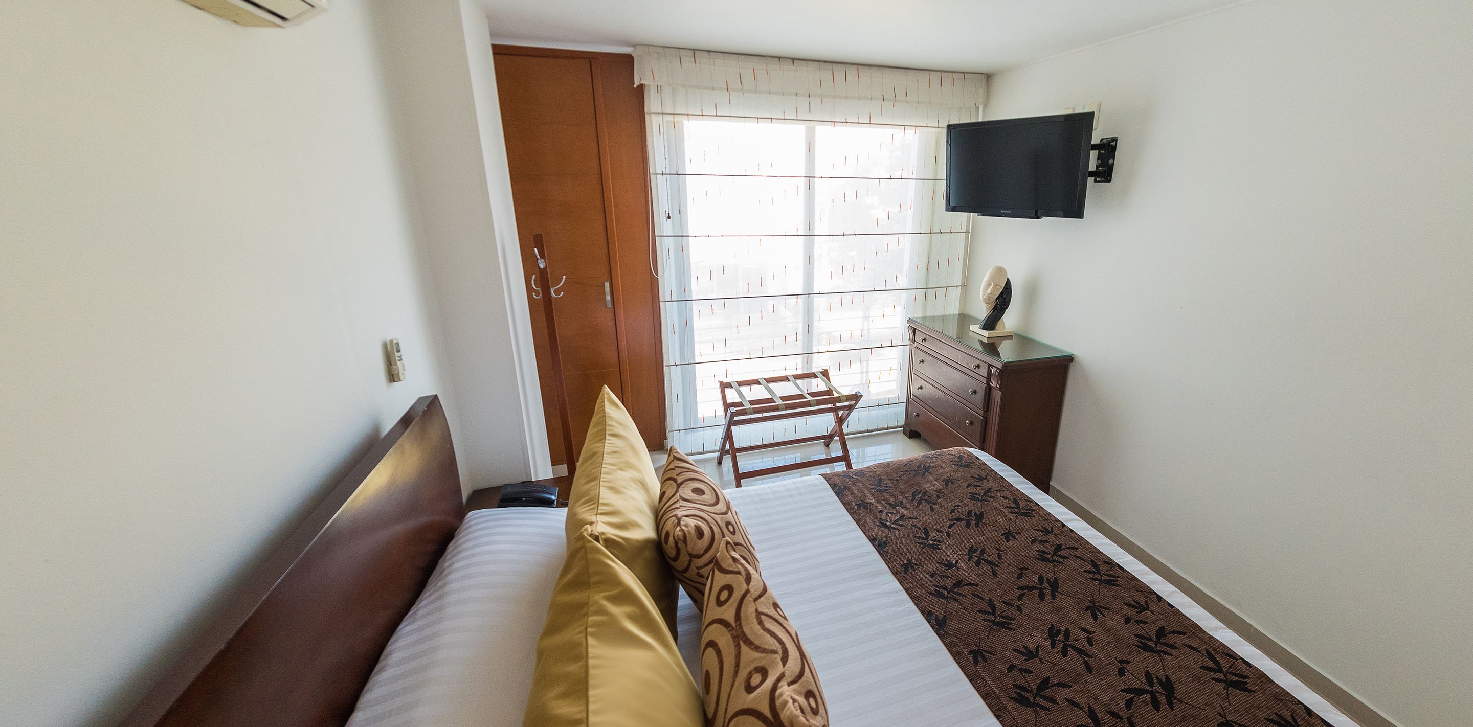 A hotel room with a bed, a dresser, a television, and a window with curtains.
