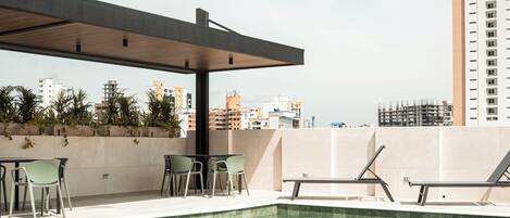 Una piscina en la azotea con sillones de descanso y una pérgola, rodeada de edificios de la ciudad.