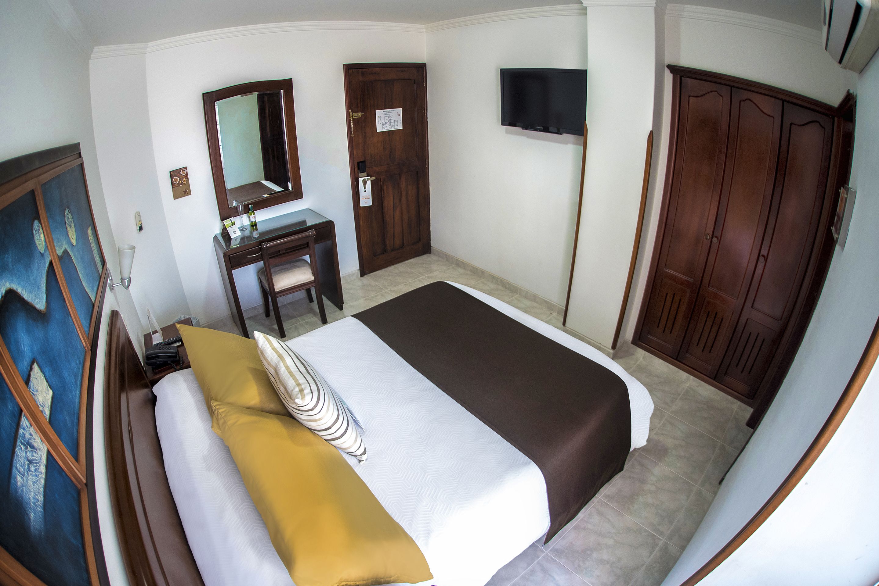 A hotel room with a bed, a desk, a mirror, a wardrobe, and a television.