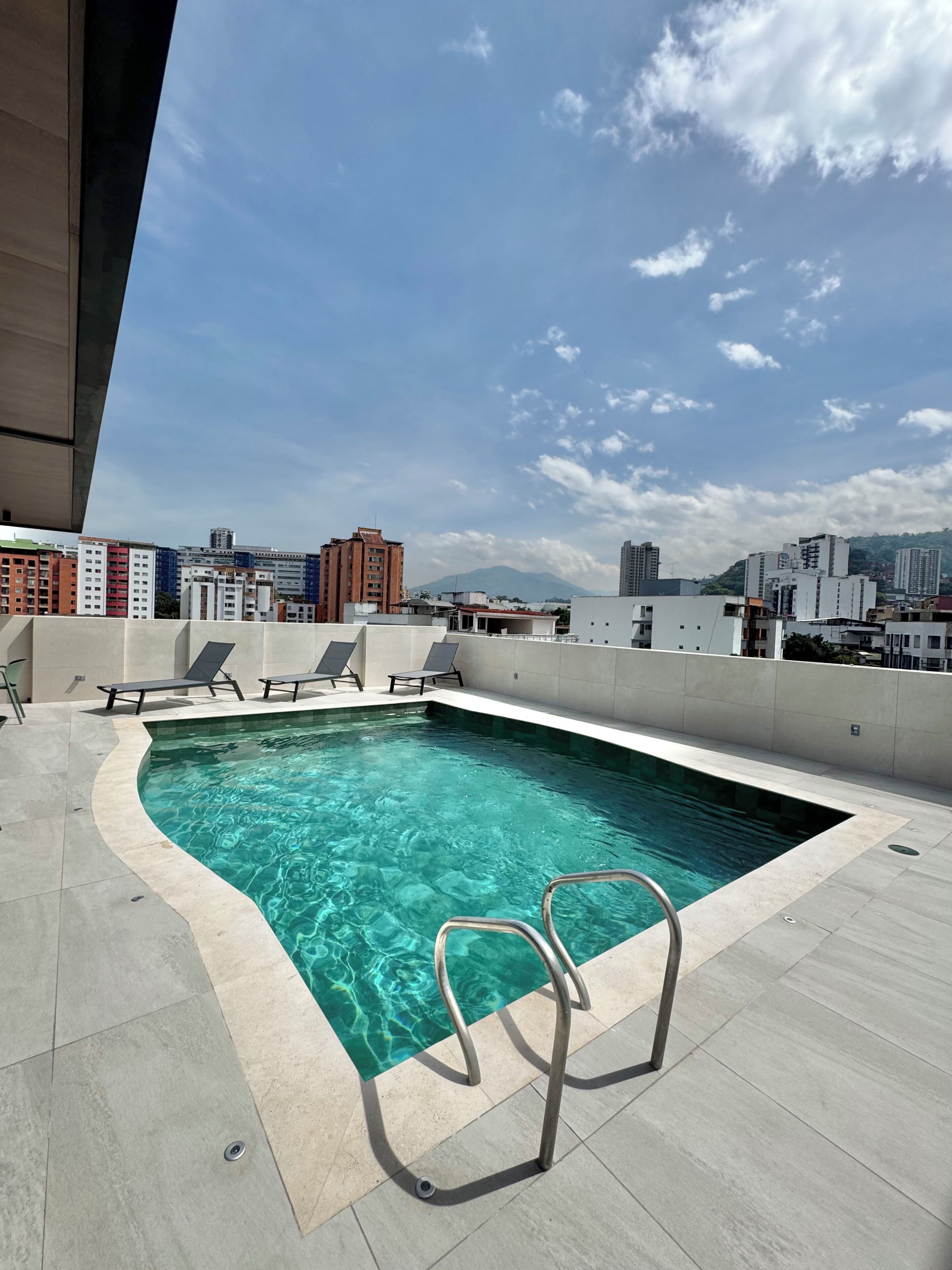 A rooftop pool with clear water, surrounded by lounge chairs and a metal ladder.