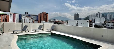 A rooftop pool with clear water, surrounded by lounge chairs and a metal ladder.