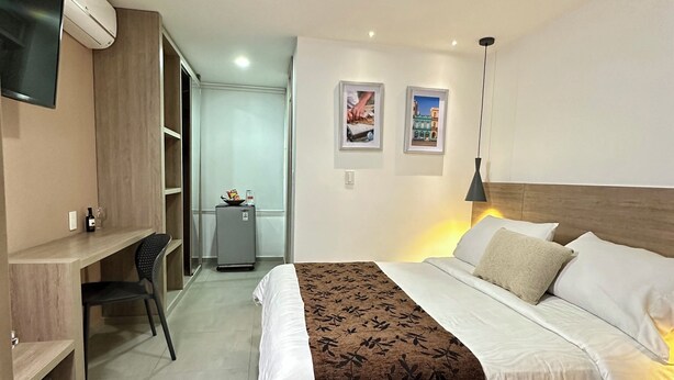 Una habitación de hotel moderna con cama, escritorio, silla, televisor, obras de arte y armario.