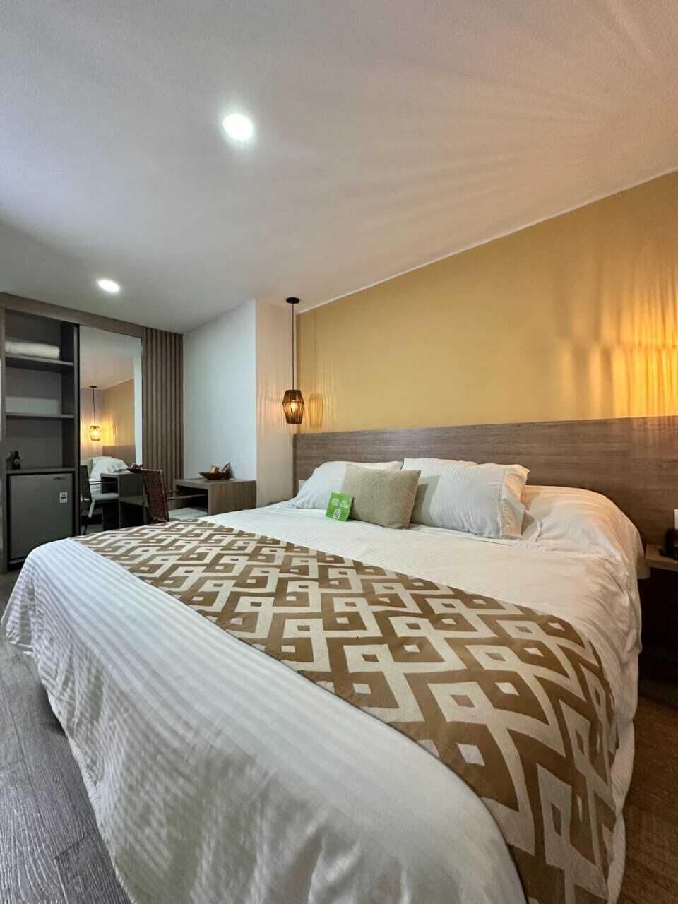 A hotel room with a large bed, a desk, a chair, and a wardrobe.