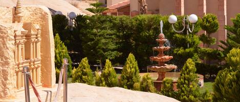 A landscaped area with a fountain, trimmed hedges, and a large rock structure.