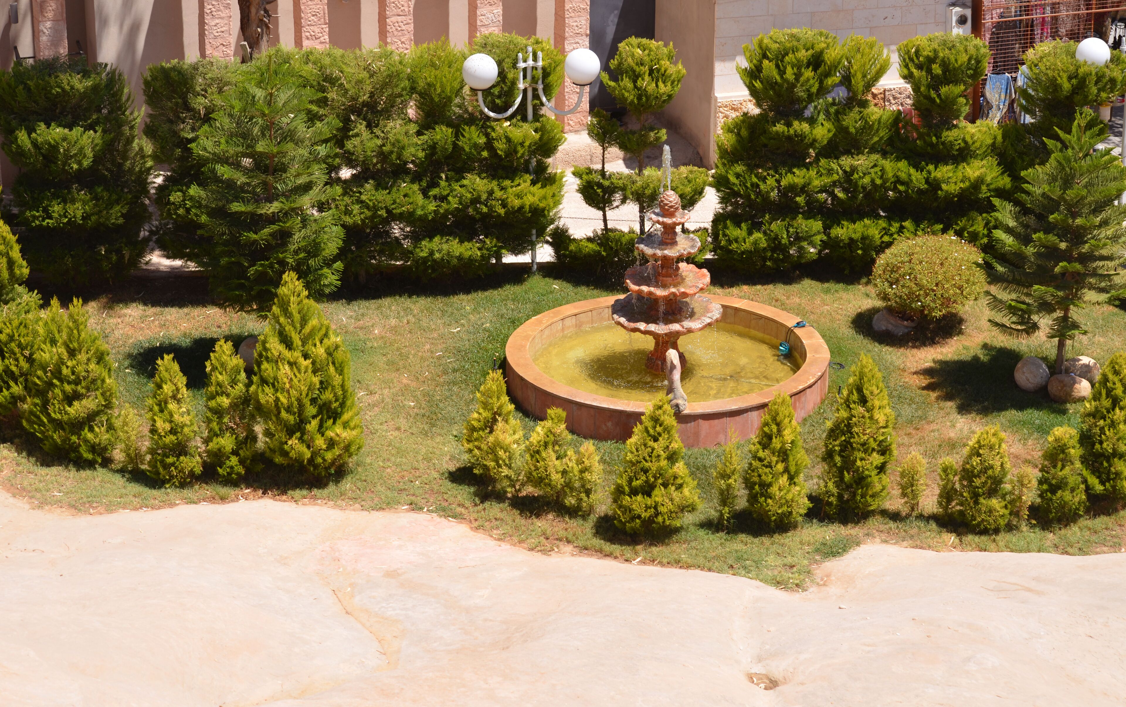 Um jardim ajardinado com uma fonte central, rodeado por árvores e arbustos bem cuidados.
