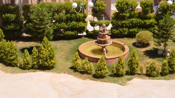 Um jardim ajardinado com uma fonte central, rodeado por árvores e arbustos bem cuidados.