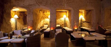 Un espacio de spa con paredes de piedra, varios rincones de descanso e iluminación ambiental.