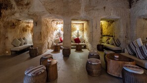 A cozy interior with stone walls, a sofa set, and round wooden stools. - Petra Guest House (Wadi Musa)