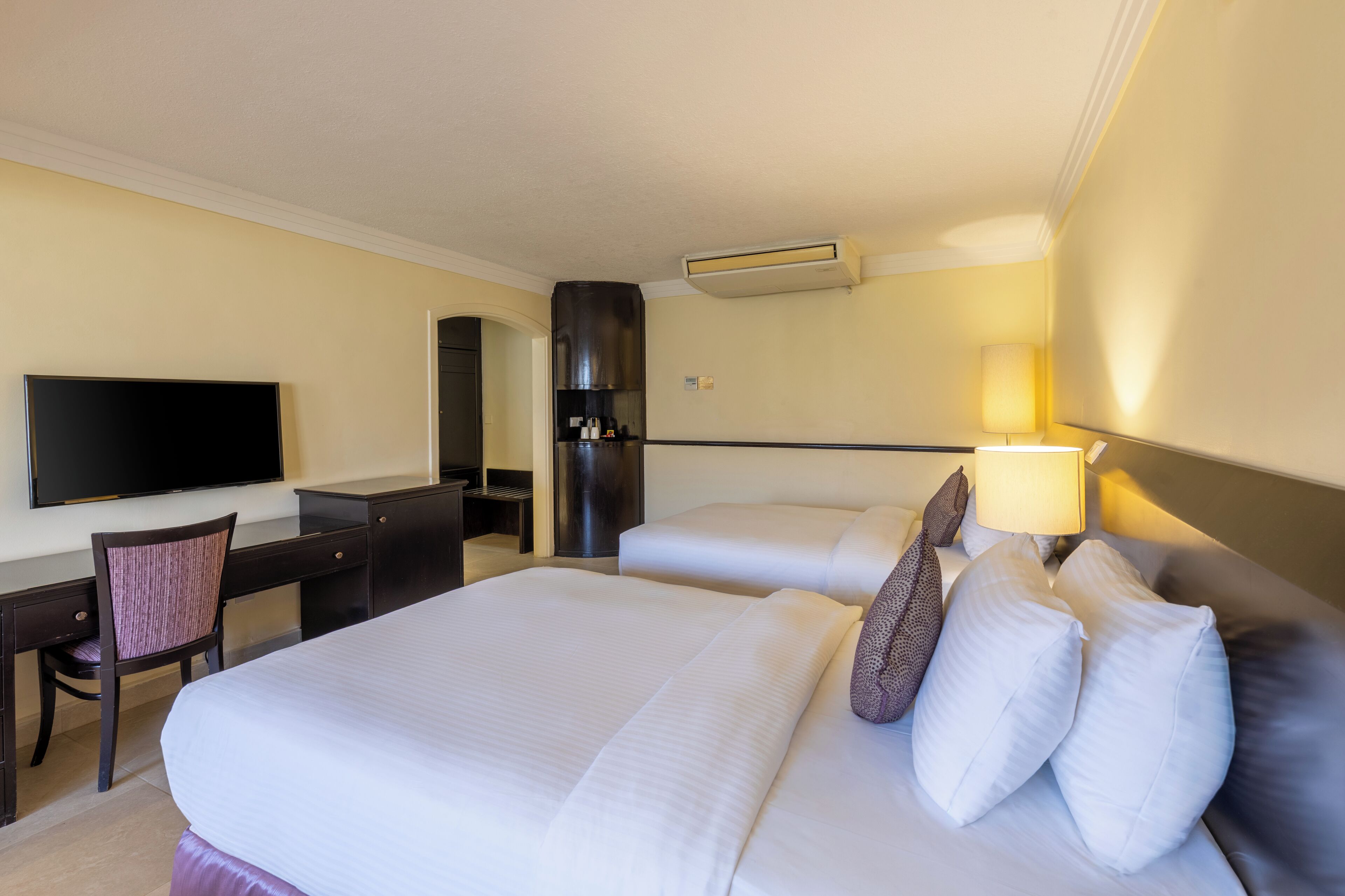 A hotel room with two beds, a desk, a TV, and a minibar.