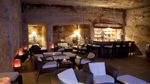 A cozy, dimly lit lounge area with wicker furniture and candles, featuring a rustic stone wall and a bar in the background. - Petra Guest House (Wadi Musa)