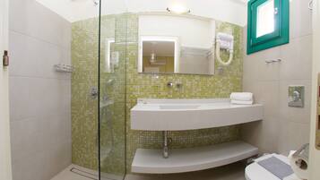 Une salle de bain dotée d’une douche à parois de verre, d’un lavabo blanc avec un miroir au-dessus, et de toilettes équipées d’un siège bidet.