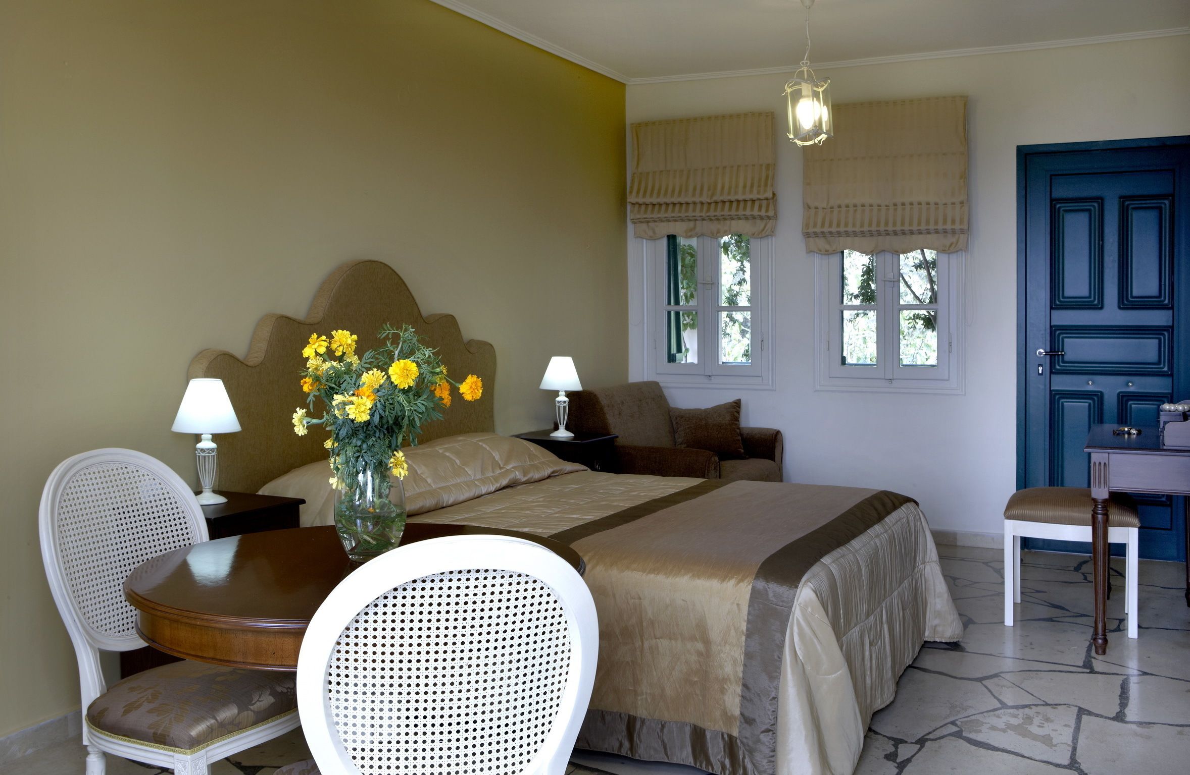 A bedroom with a bed, two bedside tables with lamps, a chair, a desk with a chair, and a window with curtains.