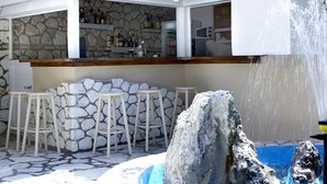 A bar area with stone walls, bar stools, and a waterfall feature. - Dafnoudi (Kefalonia)
