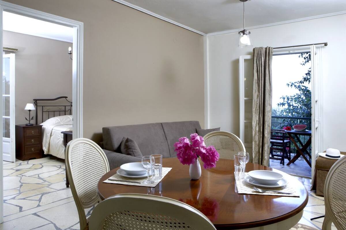 Un comedor con una mesa redonda para dos personas, un florero con flores y vistas a un balcón con mobiliario exterior.