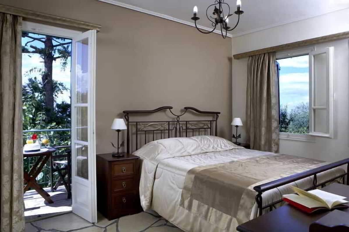Une chambre à coucher comprenant un lit, des lampes de chevet, une table de chevet, une fenêtre avec des rideaux et un balcon avec une table et des chaises.