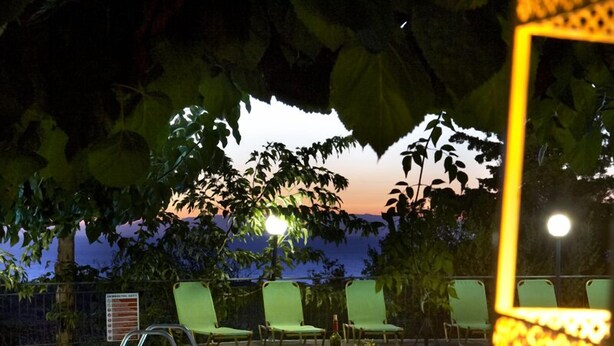 An outdoor swimming pool with a table and chairs, surrounded by greenery and a sunset view. - Dafnoudi (Kefalonia)