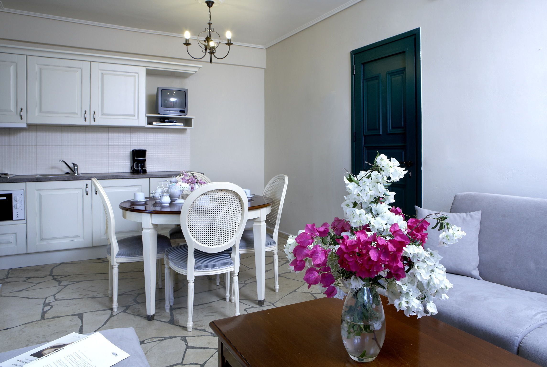 A modern kitchen with white cabinets, a dining table with chairs, a coffee maker, and a vase with flowers on the table.