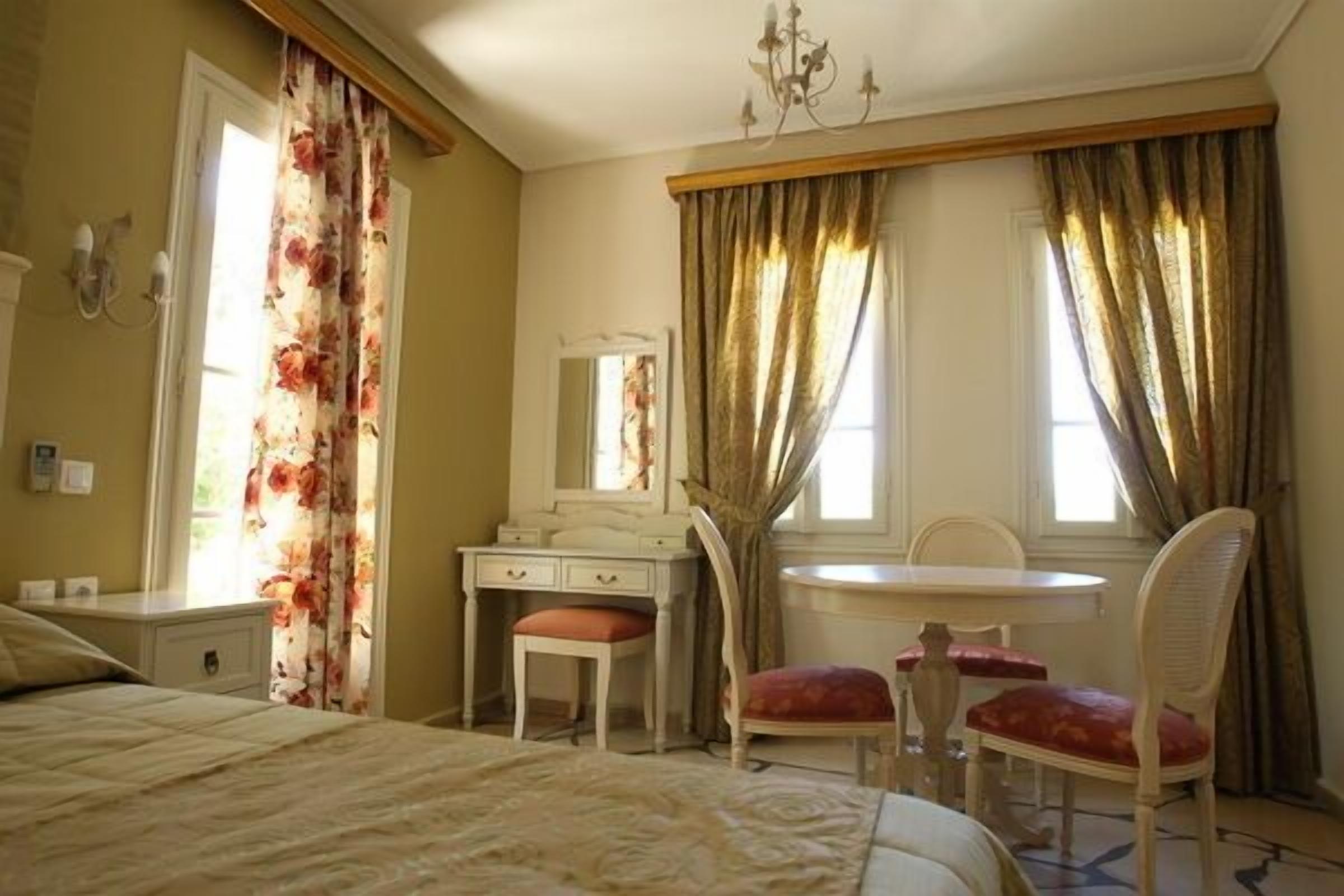 A bedroom with a bed, a vanity with a mirror, a chair, and a table.