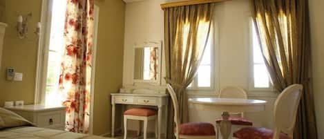 A bedroom with a bed, a vanity with a mirror, a chair, and a table.