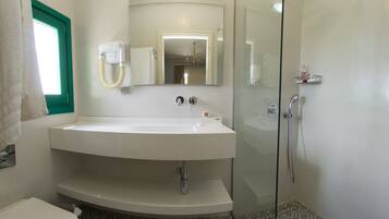 A bathroom with a white sink, a mirror, a shower, and patterned floor tiles.