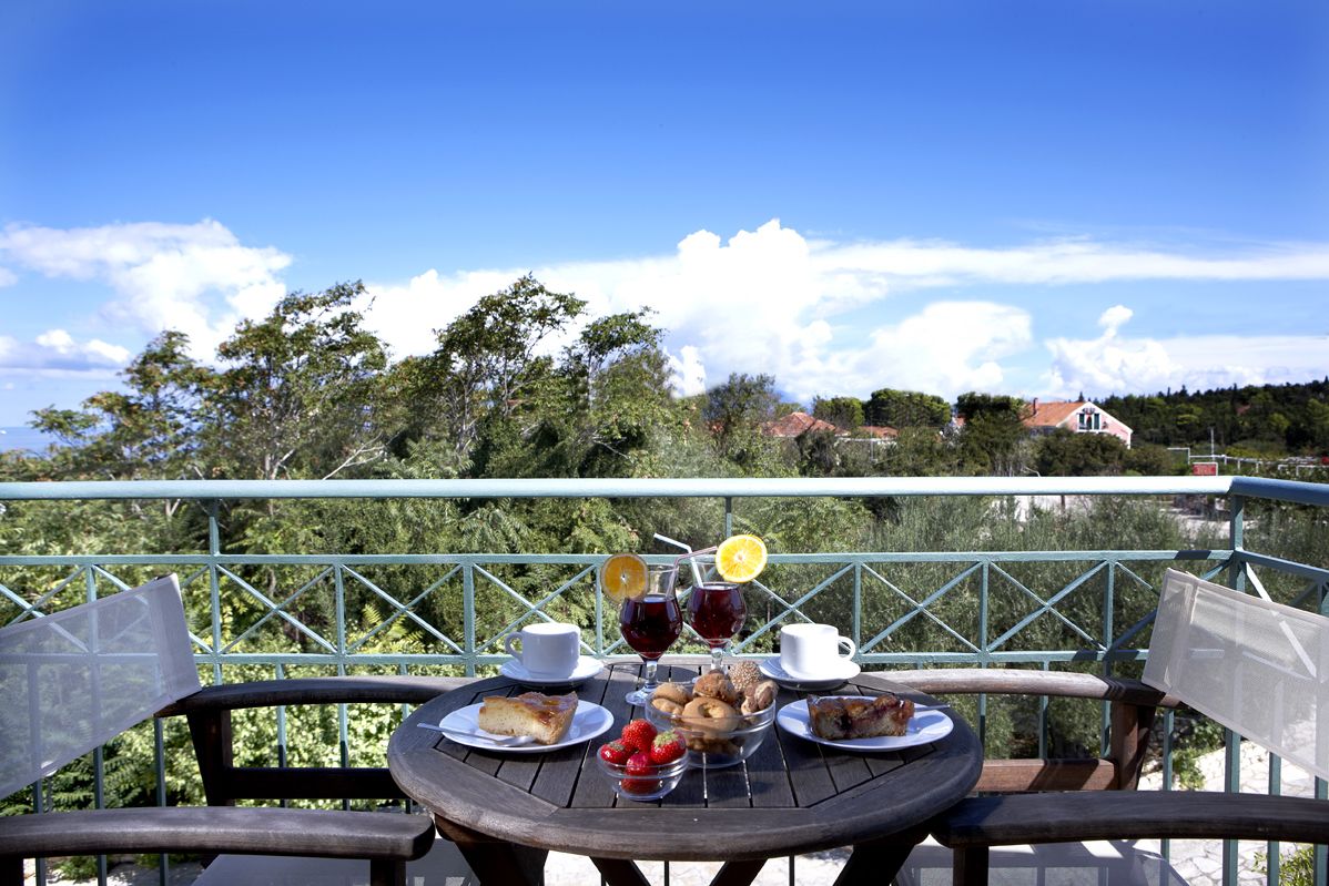 A table set with food and drinks on a balcony with a view of trees and houses.