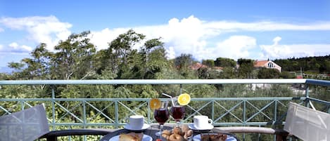 A table set with food and drinks on a balcony with a view of trees and houses.