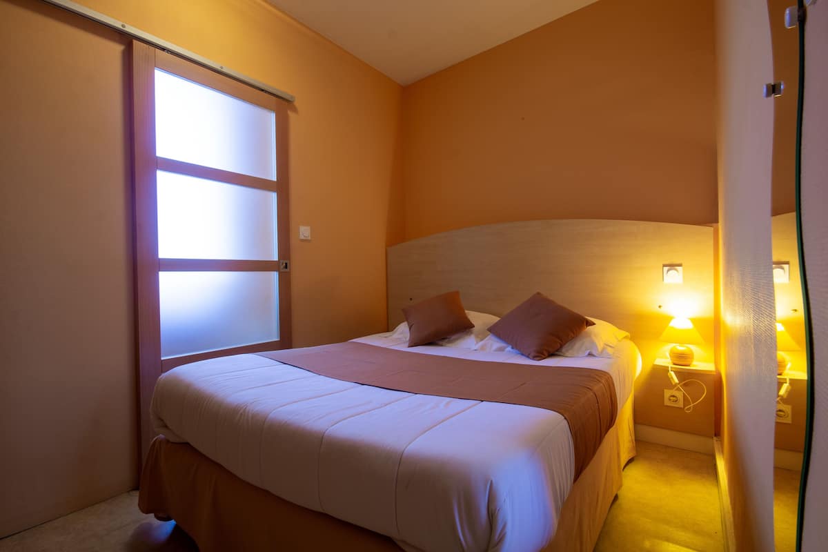 Un dormitorio con cama, almohadas, una mesita de noche y una lámpara de pared.
