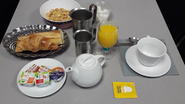 Ein Frühstückstisch mit verschiedenen Speisen, darunter Croissants, Joghurt und einer Obstschale.