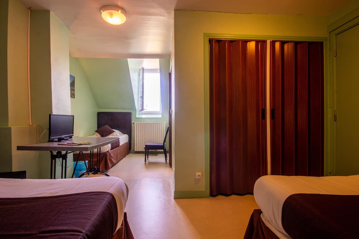 Una habitación de hotel con dos camas, un escritorio con ordenador, una silla y una ventana con cortinas.