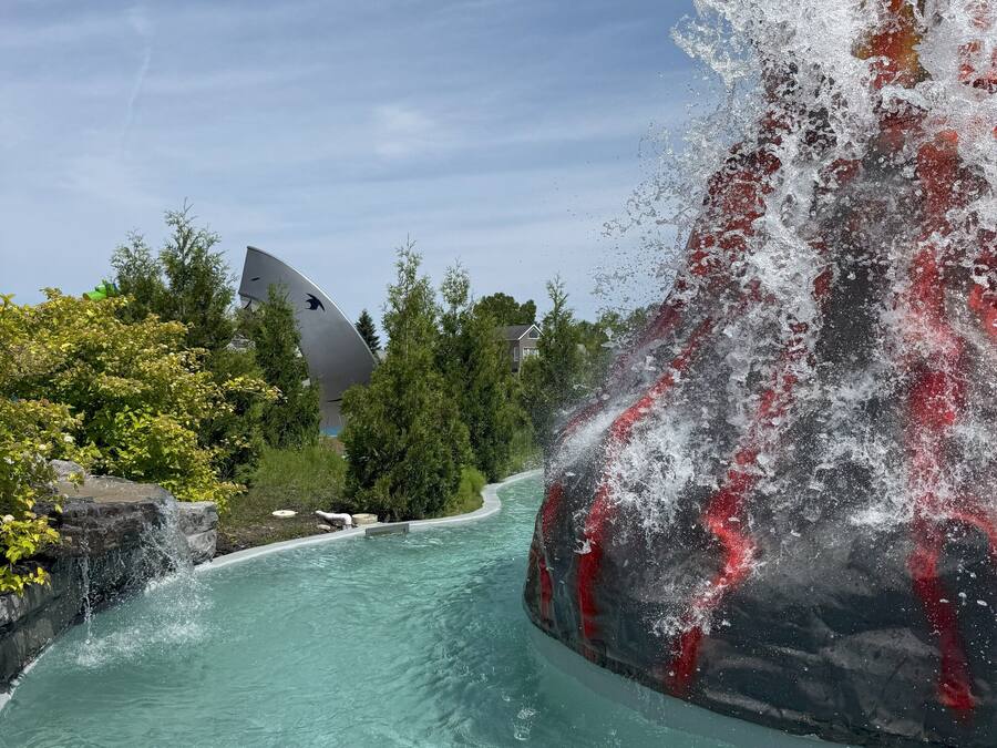 A clear pool with a waterfall feature, surrounded by greenery and a modern building.