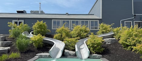 A swimming pool with two slides, surrounded by landscaping and a building in the background.