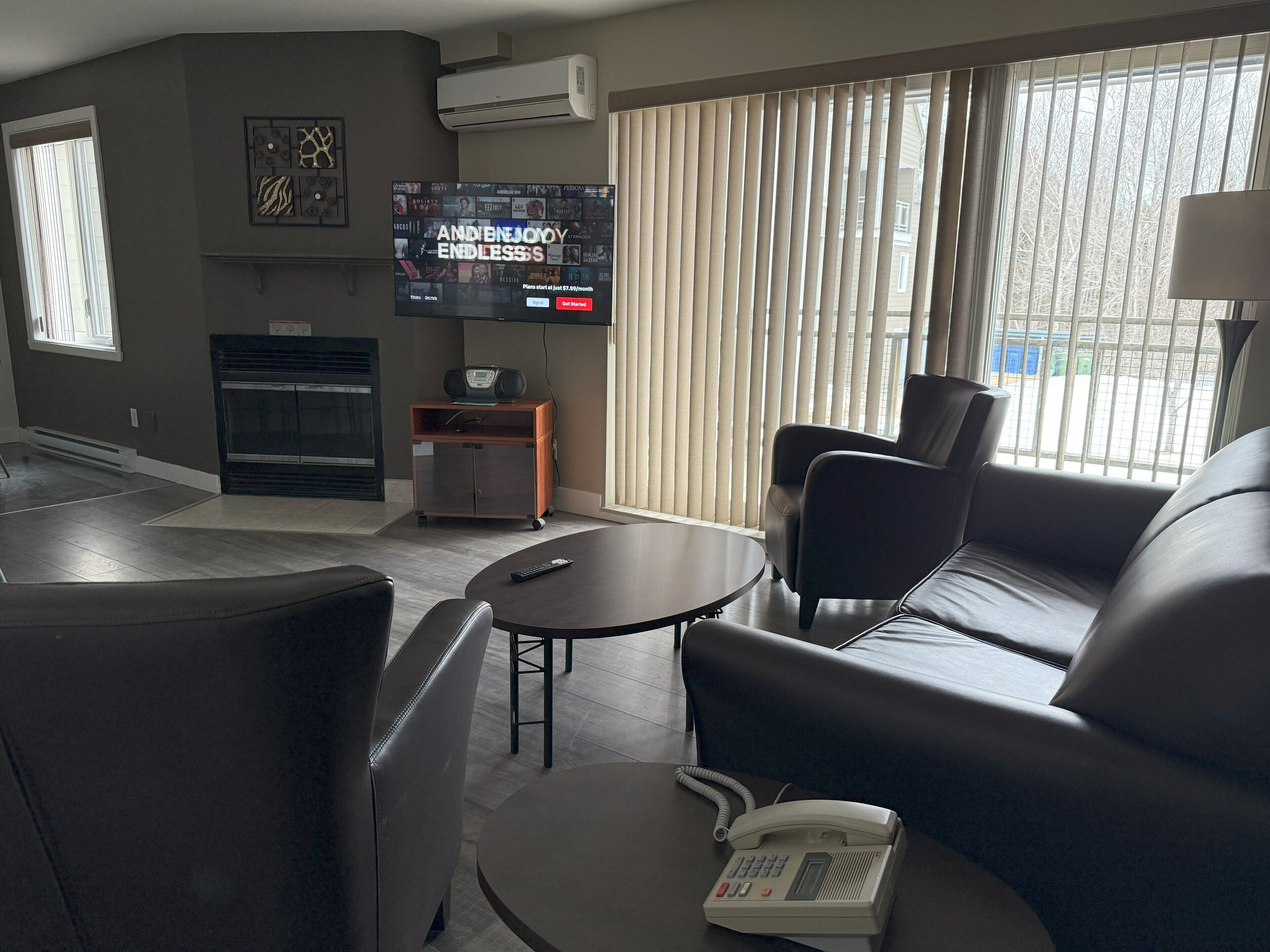 A modern hotel room with a flat-screen TV, a sofa, a coffee table, a telephone, and a fireplace.